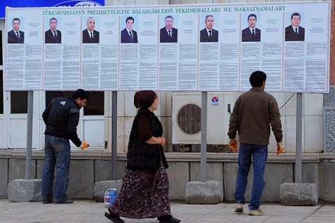 People are seen in front of a board displaying portraits of presidential candidates in Ashgabat