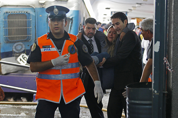 Commuters help a passenger who was injured when a commuter train crashed into the Once train station at rush hour in Buenos Aires