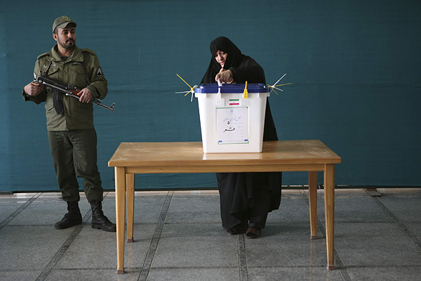 A woman casts her vote as a policeman stands guard during the parliamentary election, in the court yard of the holy shrine in Qom, south of Tehran
