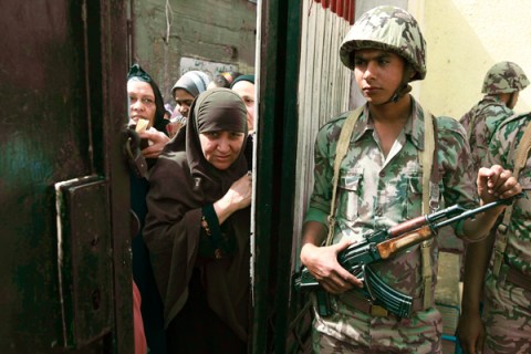 A soldier stands at the entrance to a polling station as people wait outside in Cairo