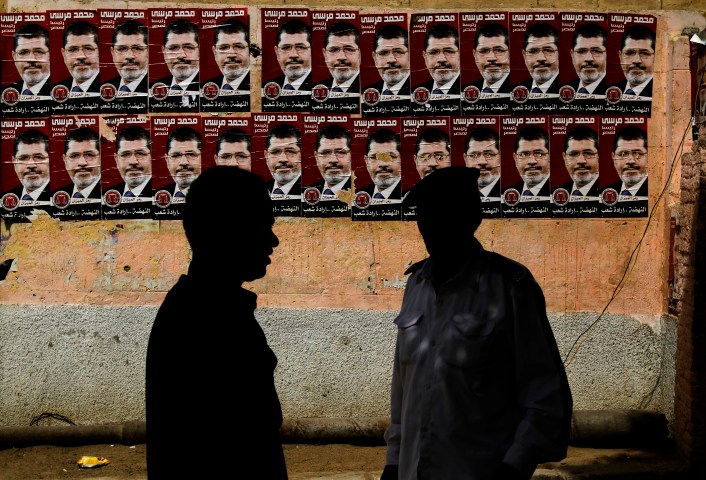 image: An Egyptian policeman and a voter stand by posters of presidential election candidate Mohamed Morsi outside a polling station in Cairo, May 24, 2012.