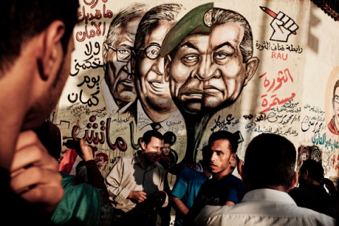 People walk under a grafitti depicting ousted president Hosni Mubarak, right.