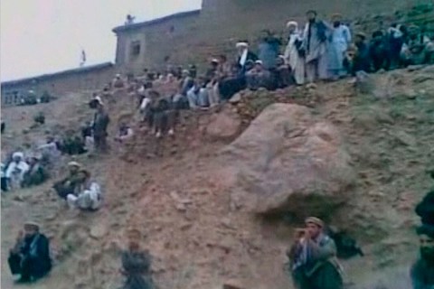 Men watch as an alleged member of the Taliban fires his rifle at a woman accused of adultery in this still image taken from undated footage released July 7, 2012.