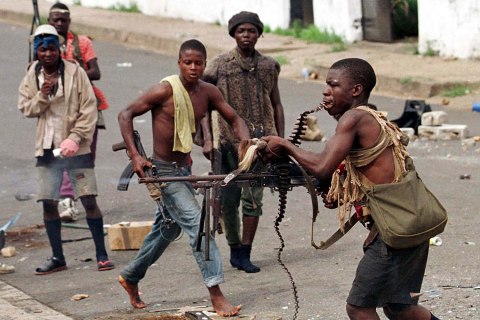 A street fighter with Charles Taylor's NPFL fires his machine gun while holding the string of bullet..