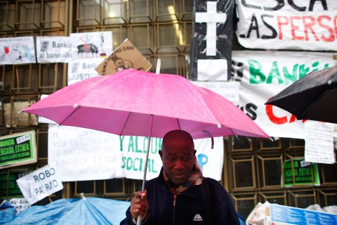A member of the Mortgage Victims' Platform awaiting an eviction order, stands under an umbrella outside Bankia bank headquarters in Madrid