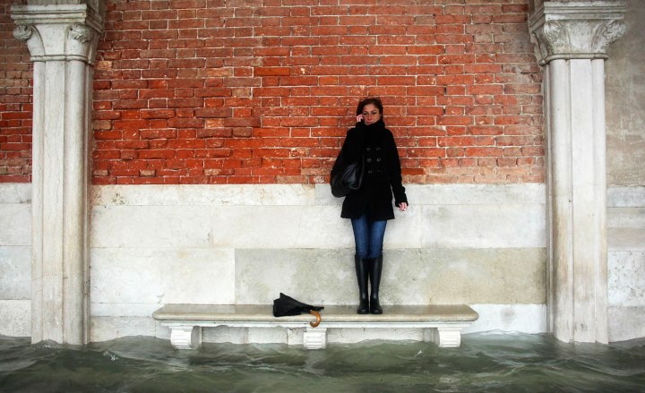 A woman stands on a bench above a flooded street during a period of high water