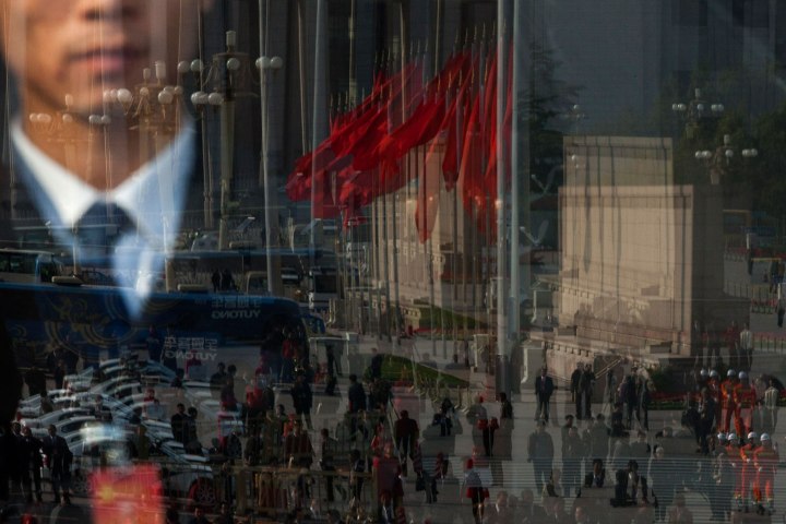 Journalists, firemen, buses, and red flags on Tiananmen are reflected in a glass door of the Great Hall of the People