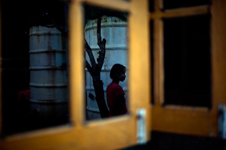 Reflected in a window, a six-year-old girl Myat Noe Thu, stands alone