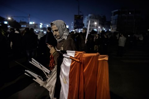 image: A street vendor holds a bunch of Egyptian flags for sale while supporters of Egypt's opposition take part in a demonstration in front of the Presidential Palace in Cairo, Dec. 18, 2012.