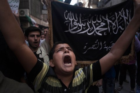 image: A Syrian shouts slogans against the regime in front of a flag of the armed Islamic opposition group al-Nusra front during a demonstration in the Bustan al-Qasr neighborhood of Aleppo, Sept. 21, 2012. 