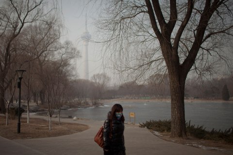 image: A woman wears a mask while walking in a park near the China Central Television Tower, background, on a hazy day in Beijing, Jan. 14, 2013. 