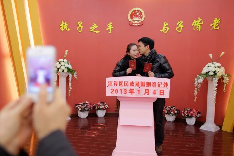 A bridegroom kisses his wife as they pose for pictures under the Chinese national emblem after having their marriage registered at a civil affairs branch office in Wuhan