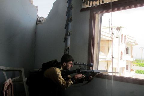A Free Syrian Army sniper takes position in a damaged house in Idlib