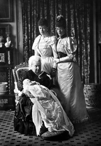Queen Victoria sits with her grandson the baby Prince Edward (later King Edward VIII) on her knee on his christening while Alexandra and Mary stand behind them. (possibly 1894)