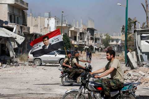 Forces loyal to Syria's President Assad carry the national flag as they ride on motorcycles in Qusair