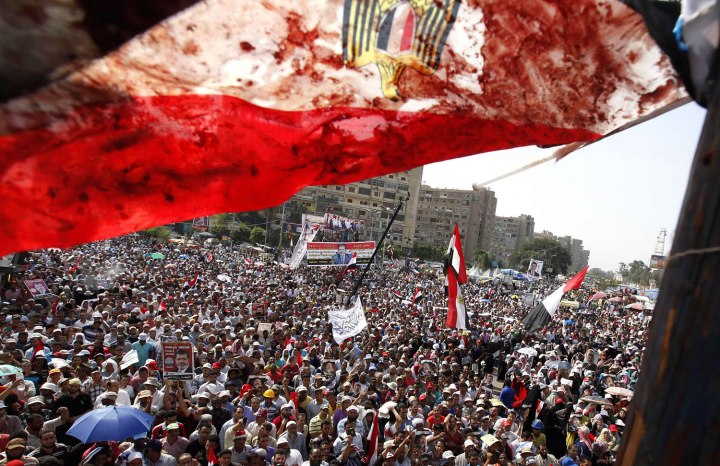 An Egyptian flag stained with blood flutters over members of the Muslim Brotherhood and supporters of deposed Egyptian President Mohamed Morsi as they shout slogans during a protest outside Raba El-Adwyia mosque in Cairo, on  July 8, 2013, following clashes in front of the Republican Guard headquarters.
