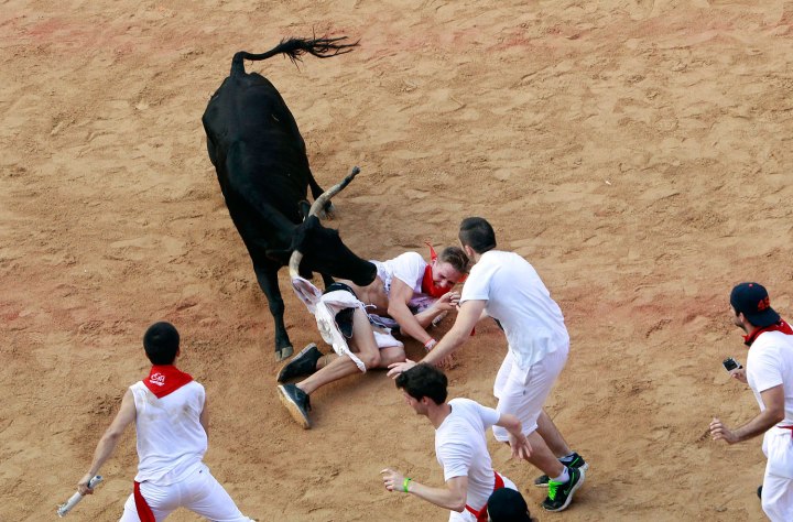 A wild cow rips the pants of a reveller after the fifth running of the bulls of the San Fermin festival in Pamplona