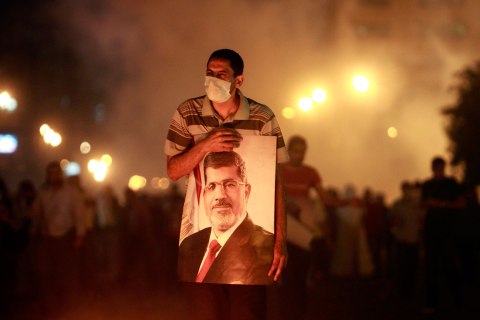 An injured supporter of deposed Egyptian President Mohamed Morsi carries a poster of Morsi as they run from tear gas fired by riot police during clashes on the Sixth of October Bridge over the Ramsis square area in central Cairo, July 15, 2013