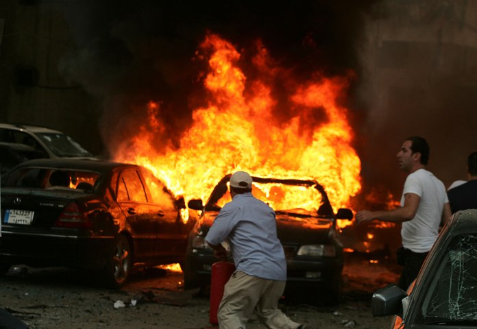 Men try to extinguish fire from burning cars at the site of an explosion, in Beirut's southern suburbs