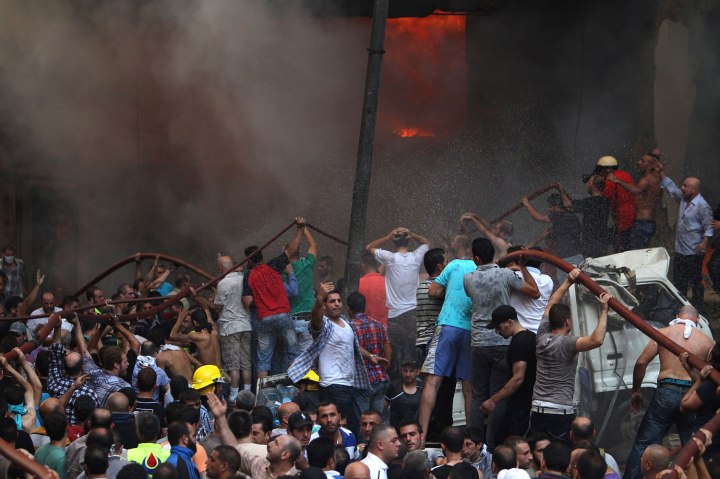 Hezbollah supporters react as they try to extinguish a fire at the site of an explosion in Beirut's southern suburbs