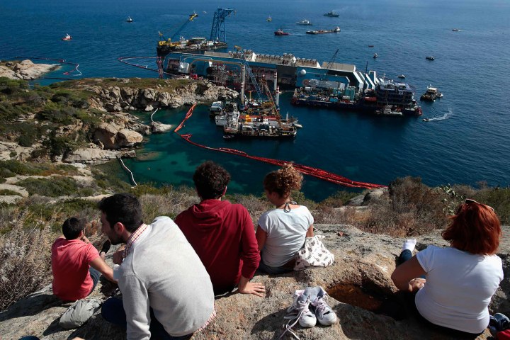 People look on as the capsized cruise liner Costa Concordia lies on its side next to Giglio Island