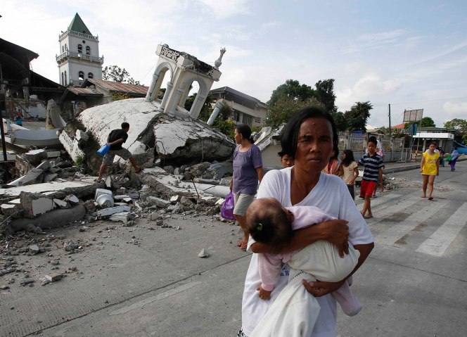 A woman carries her baby past a destroyed church belfry in Tubigon
