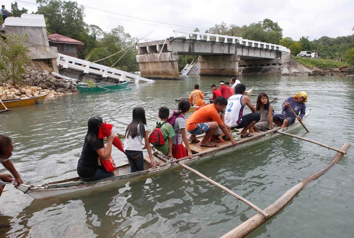 Villagers ride on a boat to cross a river after a bridge was damaged in Loo