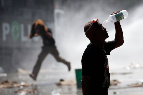 An anti-government protester recovers from teargas as another runs from water cannon during clashes with police at the barricade in front of the Government House in Bangkok