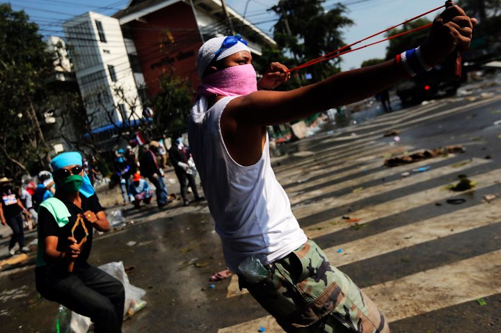 Anti-government protesters use slingshots during clashes with police at the barricade in front of the Government house in Bangkok