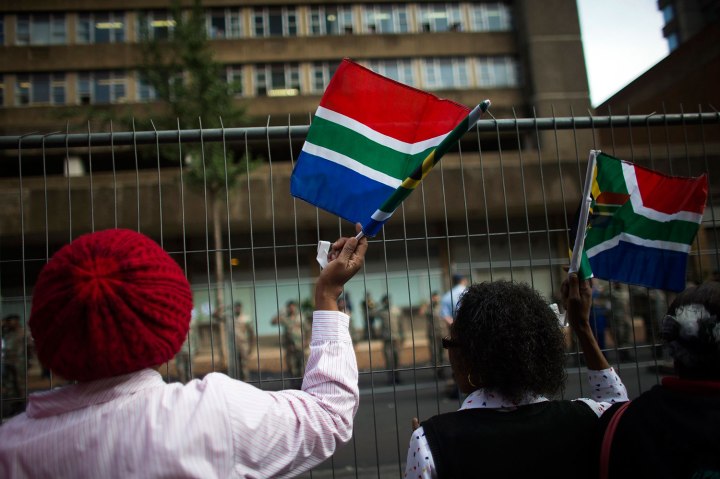 Women wave South African national flags before the cortege carrying the coffin of former South African President Nelson Mandela passes by, in the city centre of Pretoria