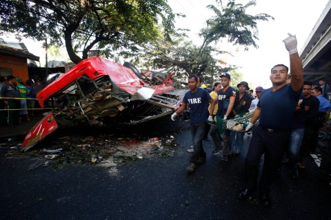 Rescuers carry a body as they walk past a bus after it fell off an elevated expressway in Manila
