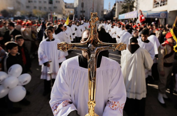 A priest holds a cross as he awaits the arrival of the Latin Patriarch of Jerusalem Fouad Twal, outside the Church of Nativity, the site revered as the birthplace of Jesus, during Christmas celebrations in the West Bank town of Bethlehem on Dec. 24, 2013. 