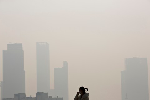 A woman wearing a mask walks on a bridge during a hazy day in downtown Shanghai