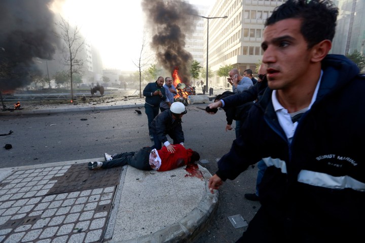 People run to help a wounded man as smoke rises from the site of an explosion in Beirut's downtown area