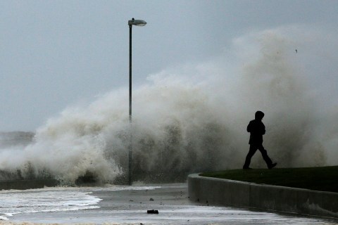 A man walks past a wave as it breaks on the promenade in Rhyl, north Wales