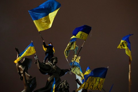 A Pro-European integration protester waves a Ukrainian national flag as she stands on a statue during a mass rally at Independence Square in Kiev