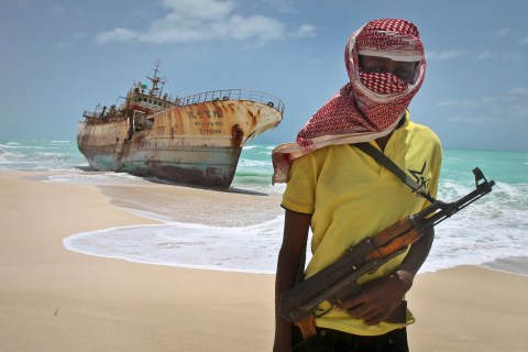 Masked Somali pirate Hassan stands near a Taiwanese fishing vessel that washed up on shore after the pirates were paid a ransom and released the crew, in the once-bustling pirate den of Hobyo, Somalia., on Sept. 23, 2012.
