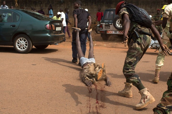 A man uses rock to strike the corpse of a man, who was killed as he was accused of joining the ousted Seleka fighters, in Bangui