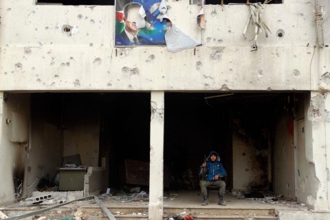 A Free Syrian Army fighter poses with his weapon under a torn picture of Hafez al-Assad, father of President Bashar Al-Assad, at the Tameko pharmaceutical factory, in eastern al-Ghouta