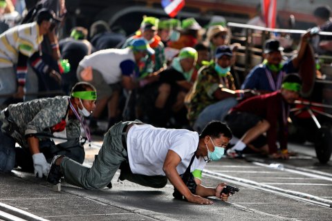 An anti-government protester crawls with his pistol during a gunfight between supporters and opponents of Thailand's government near Laksi district office in Bangkok Feb. 1, 2014.
