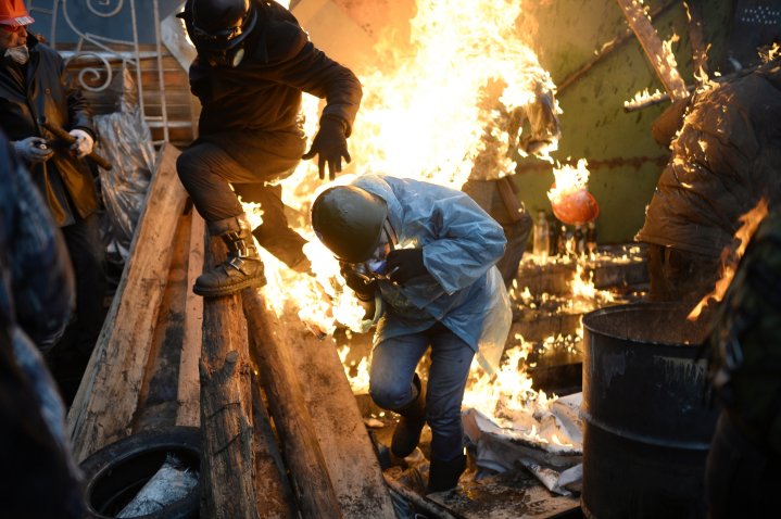 Protesters try to protect themselves from fire as they stand behind burning barricades during clashes with police on February 20, 2014 in Kiev.